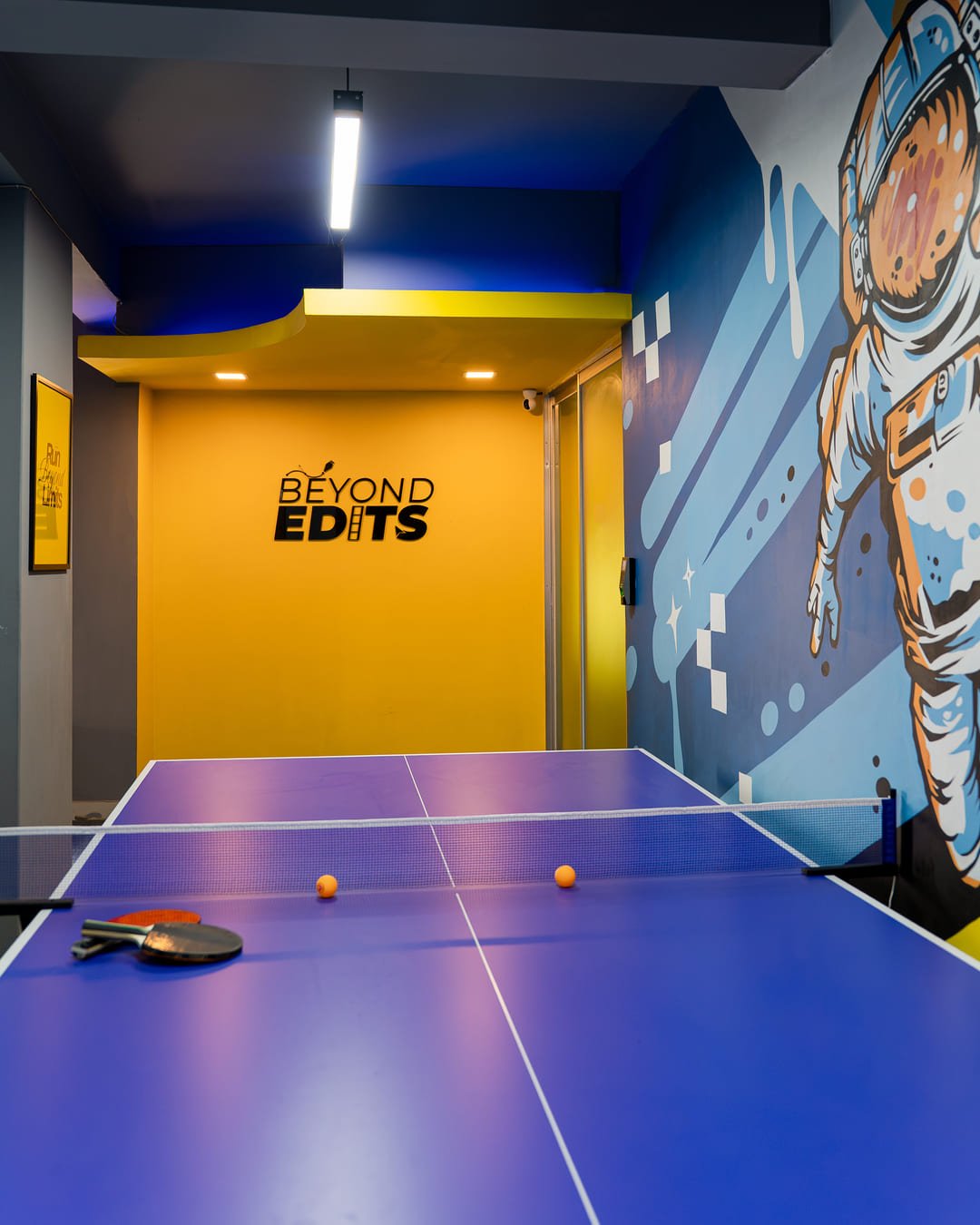 The Beyond Edits office in Dhaka, with the logo on the yellow wall and a mural beside the table
