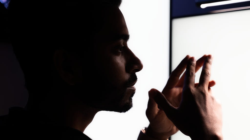 Raihan Ghorami in profile at his desk, hands raised, working through something on a monitor